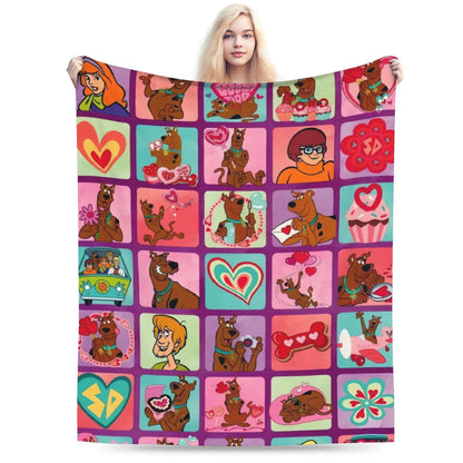 A woman holds up a large blanket featuring a colorful grid pattern of cartoon Scooby-Doo characters and Valentine-themed illustrations, set against a plain white background.