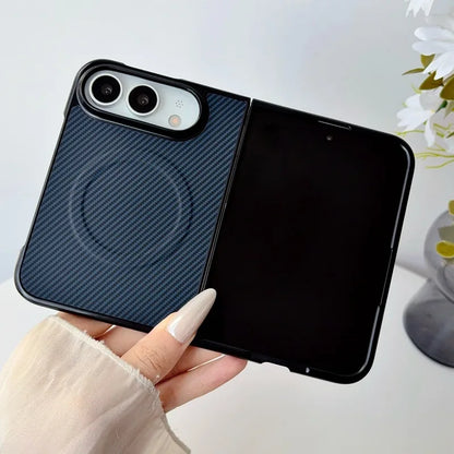 A hand holds a black foldable phone case with a dark blue carbon-fiber textured back panel and a black magnetic ring on the rear, shown against a light background with a blurred flower pot.