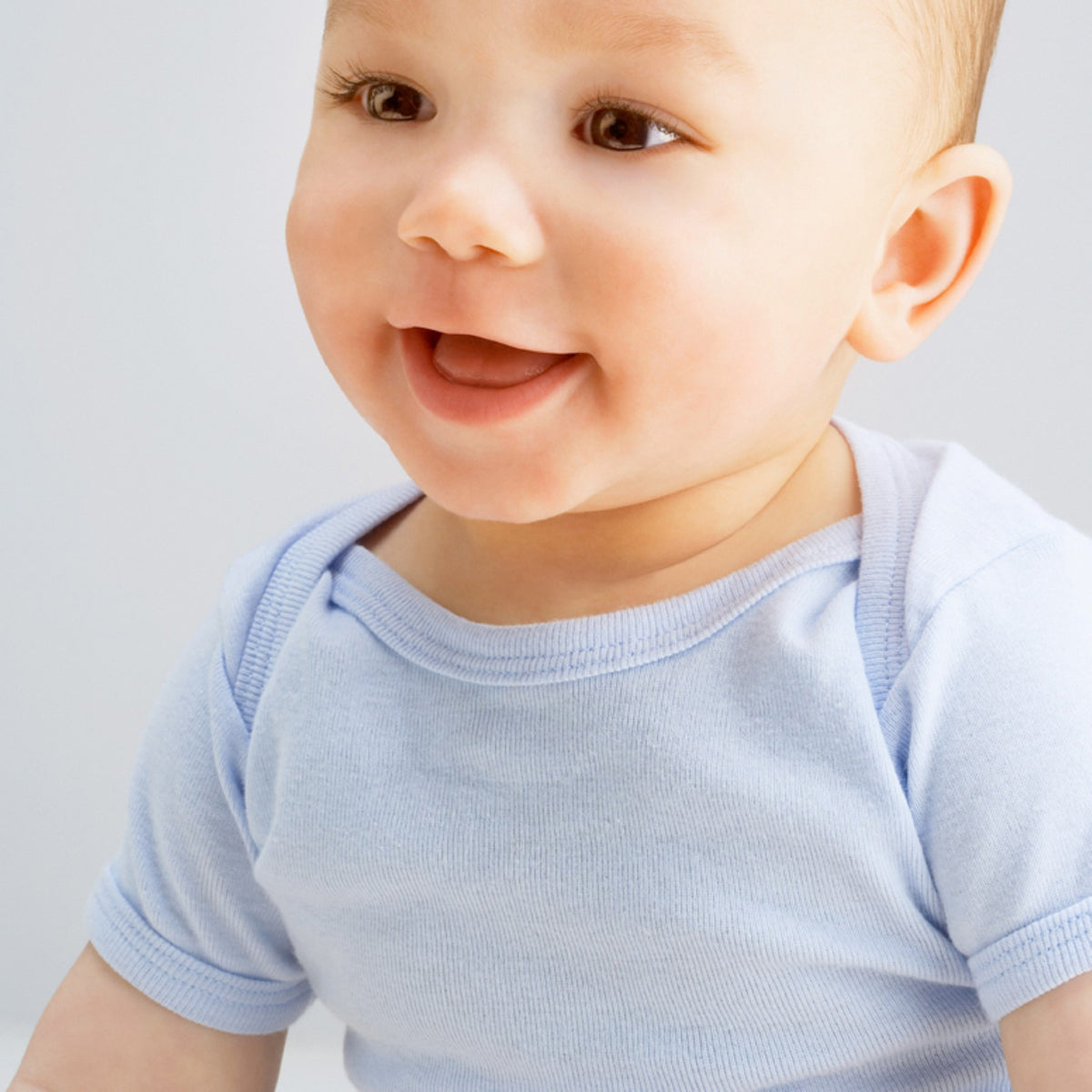 Smiling baby wearing light blue onesie showcasing Emerald Clover boys layette set 28 piece soft cotton essentials