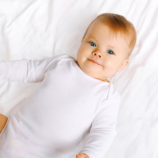 Emerald Clover newborn baby boy layette set white cotton long sleeve onesie on soft crib sheet
